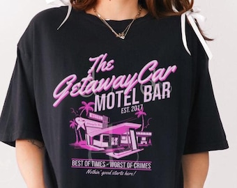 May include: A black t-shirt with a pink graphic of a motel with palm trees and the text "The Getaway Car Motel Bar Est. 2017" and the text "Best of Times - Worst of Crimes Nothin' good starts here!"