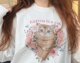 May include: White sweatshirt with a pink graphic of a cat surrounded by flowers and the text "karma is a cat".