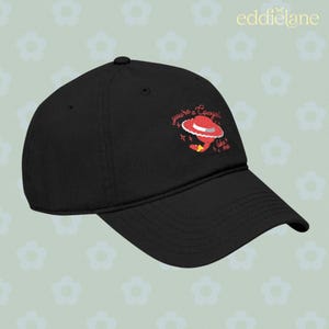 Puede incluir: Una gorra de b&eacute;isbol negra con un gr&aacute;fico bordado de un sombrero de vaquero rojo con una banda blanca y el texto "you're a cowgirl like me" en letra cursiva roja, acentuado por peque&ntilde;as formas de estrellas rojas en el panel frontal.