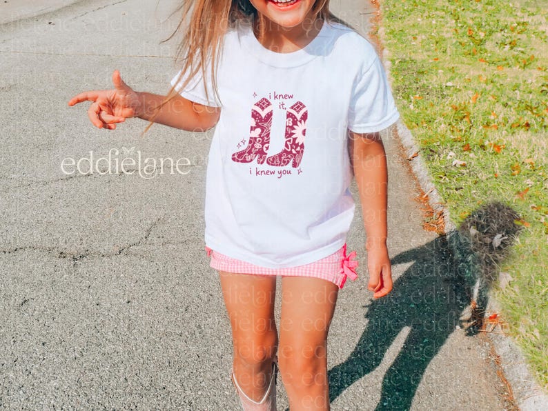 girl wearing a white t-shirt with a drawing of red cowgirl boots with a bandana print that features doodles inspired by toy story and swifties