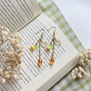 May include: A pair of dangle earrings with gold chains and clear, orange, and green glass beads. The beads are shaped like leaves and flowers.