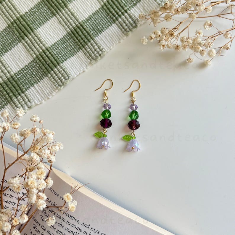 May include: A pair of dangle earrings with a flower charm. The earrings feature green, purple, and clear crystal beads.