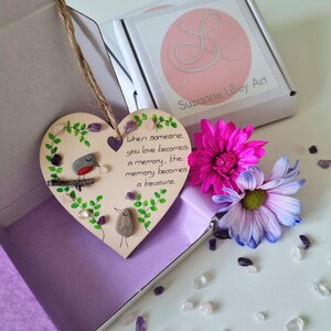 May include: A heart-shaped wooden ornament hanging by a jute twine, featuring a painted robin on a branch, green vines, and small purple and clear crystals. The text reads: When someone you love becomes a memory, the memory becomes a treasure.