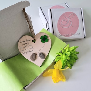 May include: A heart-shaped wooden sign with a four-leaf clover and two small birds made of stones. The sign reads "A best friend is like a four-leaf clover, hard to find and lucky to have".