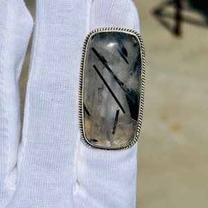 May include: A silver ring with a rectangular black and clear quartz stone. The stone has black lines running through it.