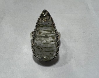 Könnte beinhalten: Ein silberner Ring mit einem tropfenförmigen, klaren Quarzstein in einer silbernen Fassung. Der Stein hat ein weißes und graues Muster.