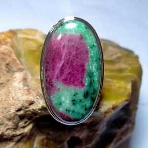 May include: A silver ring featuring a large oval green and pink gemstone. The gemstone has a mottled pattern of green and pink.