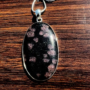Puede incluir: Un collar de cadena de plata con un colgante ovalado con una piedra moteada de color negro y rosa.