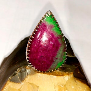 Puede incluir: Un anillo en forma de lágrima con una piedra preciosa verde y rosa engastada en un engaste de plata.