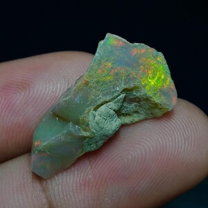 May include: A rough, green and white opal with flashes of orange and yellow. The opal is a natural stone and has a unique, irregular shape.