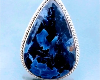 May include: A teardrop-shaped ring with a blue and black gemstone set in a silver band with a braided edge.