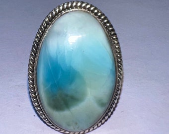 Op de afbeelding: Een zilveren ring met een ovale, blauwe en witte cabochon edelsteen. De ring heeft een touwachtig ontwerp rond de rand van de zetting.