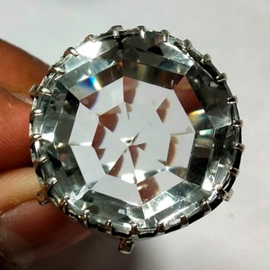 May include: A large, clear crystal with a faceted design is set in a silver-toned metal frame. The crystal is octagonal in shape and has a high polish.