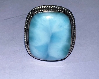 Op de afbeelding: Een zilveren ring met een lichtblauwe edelsteen. De edelsteen heeft een bewolkt, gemarmerd patroon.