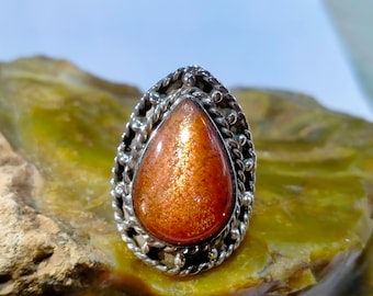 May include: A silver ring with an orange sunstone gemstone set in a teardrop shape. The ring has a detailed, ornate design.