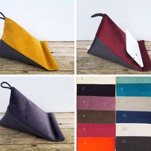 May include: A set of three triangular pillows with a gray fabric base and a velvet top. The pillows are available in mustard yellow, burgundy red, and dark gray. The pillows are designed to prop up a laptop or tablet.