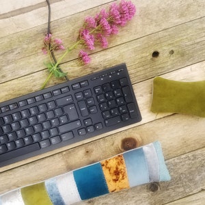 May include: A black keyboard with a numeric keypad, a green velvet cushion, and a multi-coloured fabric cushion on a wooden surface.