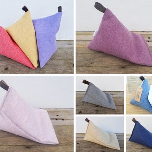 May include: Set of eight triangular reading pillows in various colours, including pink, purple, yellow, red, grey, beige, and blue. The pillows are made of a soft, textured fabric and have a leather strap handle.