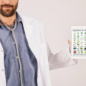 May include: A person wearing a white lab coat and a stethoscope around their neck holds a tablet displaying a chart of Vitamin K foods. The chart features various vegetables, fruits, and other food items, with the text "VITAMIN K FOODS" at the top.
