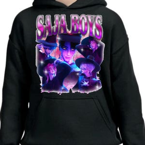 May include: Black hoodie featuring a graphic design with the text "SAJA BOYS" in a stylized, purple and pink font. The graphic includes multiple anime-style character illustrations in shades of purple, blue, and pink.