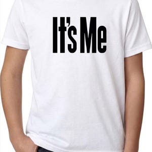 May include: A white short-sleeved t-shirt featuring the text "It's Me" printed in bold black capital letters across the center of the chest. The garment has a classic crew neckline and a standard fit, providing a clean and simple appearance.