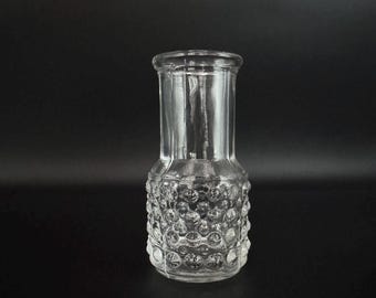 May include: A clear glass vase with a textured, bubble-like design. The vase has a cylindrical shape with a slightly wider base.