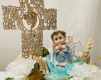 May include: A wooden cross with the Lord's Prayer in Spanish, a small angel figurine, and white flowers in a burlap-covered box with a gold ribbon and the text "Recuerda Demi Bautismo".