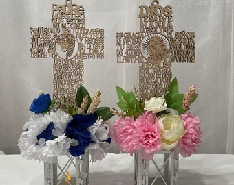 May include: Two white lanterns with floral arrangements. The lanterns have a cross-shaped design with religious text in Spanish. One arrangement features pink and white flowers, the other blue and white flowers.