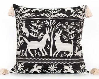 May include: Black and white throw pillow with a decorative design featuring stylized animals and plants. The pillow has tassels on each corner.