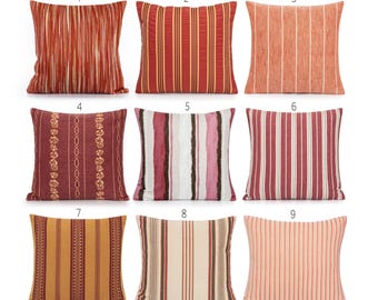May include: Nine decorative throw pillows with various striped and patterned designs. The pillows feature a range of colors, including red, orange, and gold. Some pillows have vertical stripes, while others have floral or geometric patterns.
