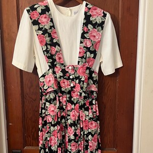 May include: A black and white floral print dress with pink roses. The dress has a white top with a scoop neck and short sleeves. The skirt is pleated and has a button closure at the waist.