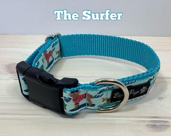Könnte beinhalten: Ein türkisblaues Hundehalsband mit einem bunten Druck von Hunden, die surfen. Das Halsband hat eine schwarze Schnalle und einen silbernen D-Ring. Der Text "The Surfer" ist über dem Halsband gedruckt und "Dog Pup" ist auf dem Halsband gedruckt.