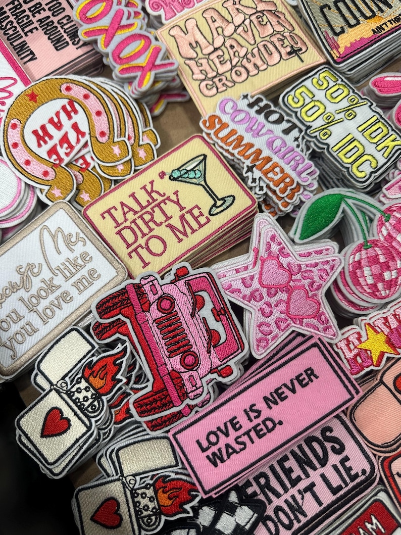 May include: A collection of embroidered patches in various shapes and colors. Designs include a horseshoe, martini glass, jeep, star, and text phrases like "Talk Dirty To Me" and "Love Is Never Wasted."