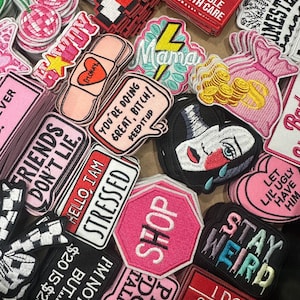 May include: A collection of embroidered patches in various shapes and colors. Patches include phrases like "Stay Weird," "Hello, I am Stressed," and "Shop." Other designs feature a crying face, a heart, and a cat.