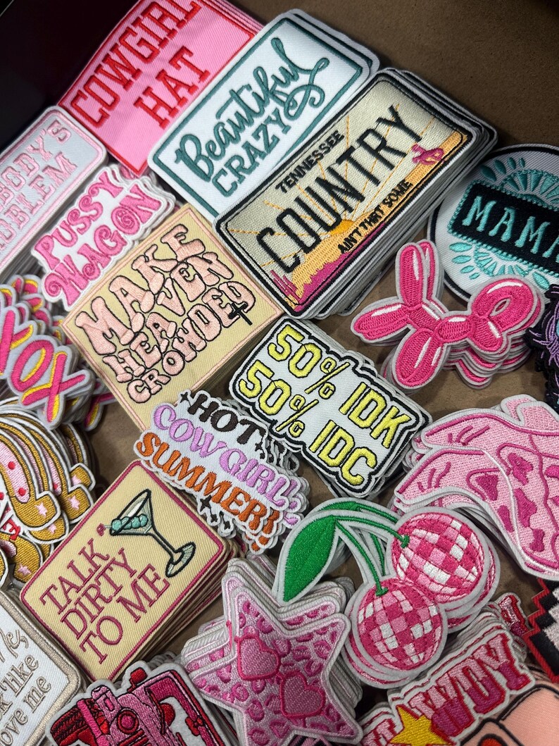 May include: A collection of embroidered patches with various designs and text. The patches feature phrases like "Beautiful Crazy," "Country," and "Talk Dirty to Me." Colors include pink, white, yellow, and green. The patches are likely for clothing or accessories.