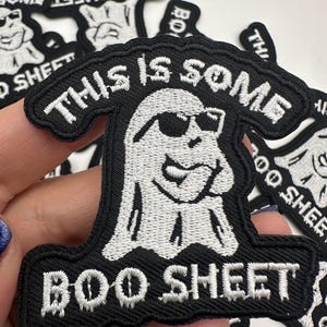 May include: Black and white embroidered patch featuring a cartoon ghost wearing sunglasses. The patch reads "THIS IS SOME BOO SHEET" in white lettering. Several patches are visible.
