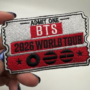 May include: Embroidered patch in the shape of a ticket, featuring the text "ADMIT ONE" at the top. The patch has a red rectangle with "BTS" and "2026 WORLD TOUR" in white. Black symbols and stars are also present.