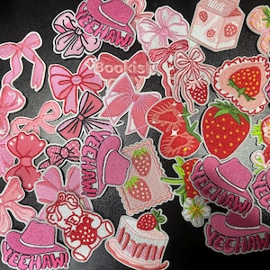 May include: A collection of pink embroidered patches featuring bows, strawberries, cowboy hats with "YEEHAW!" text, and a strawberry cake. The patches vary in size and design, with a white border.