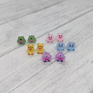 May include: A set of ten colorful monster earrings. The earrings are made of plastic and feature different colors and designs, including green, yellow, pink, and blue.