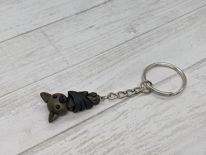 May include: A brown and black bat-shaped keychain with a silver chain and ring.
