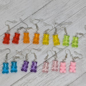 May include: A set of 10 pairs of gummy bear earrings in various colors, including red, orange, yellow, green, blue, purple, and pink. The earrings are made of clear plastic and have a silver hook.