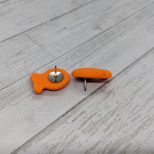 May include: Two orange fish-shaped push pins with silver push pins.