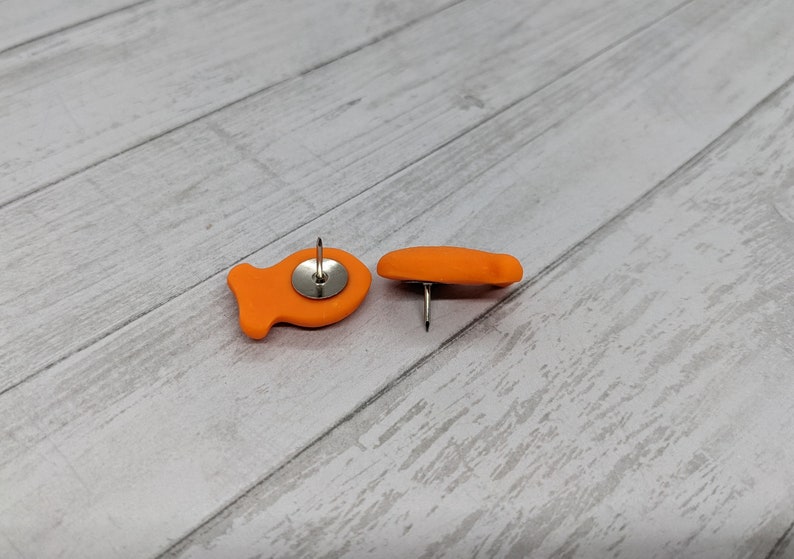 May include: Two orange fish-shaped push pins with silver push pins.