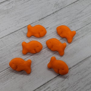 May include: Six orange goldfish crackers on a light wood surface.