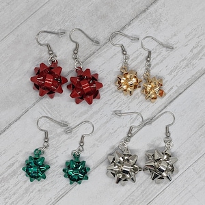 May include: A set of six bow earrings in red, gold, silver, and green. The earrings are made of metal and have a bow shape. They are a fun and festive accessory for any occasion.