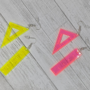 May include: A pair of neon yellow and pink ruler earrings. One earring is a triangle ruler and the other is a rectangular ruler.