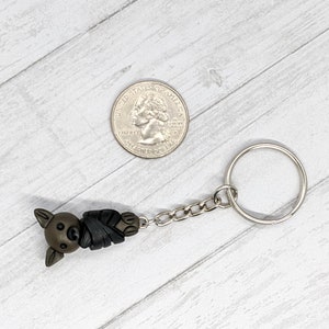 May include: A brown and black bat-shaped keychain with a silver chain and ring. The keychain is about the size of a US quarter.