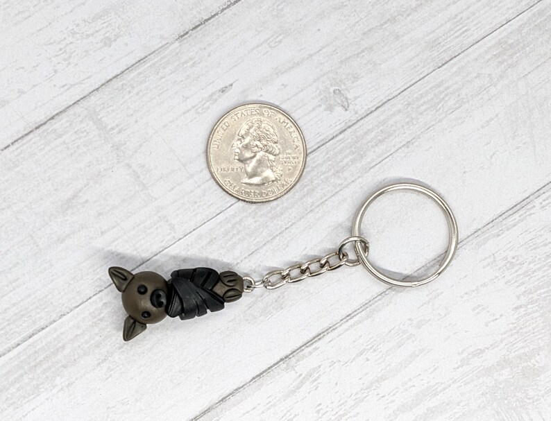 May include: A brown and black bat-shaped keychain with a silver chain and ring. The keychain is about the size of a US quarter.