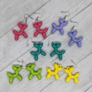 May include: A set of eight balloon dog earrings in various colors, including pink, purple, teal, green, and yellow. The earrings are made of polymer clay and have silver hooks.