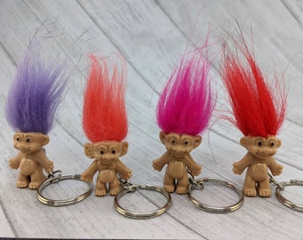 May include: Four troll keychain figurines with different colored hair. The trolls are all wearing keychains. The trolls have purple, orange, pink, and red hair.